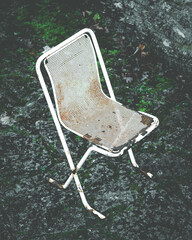 Old, rusty metal chair on stone background. Scenic, white, abandoned outdoor beach cafe furniture. Dark, moody, creepy, artistic portrait. Loneliness, emptyness, oldness, senility concept. Close up