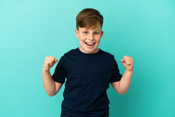 Little redhead boy isolated on blue background celebrating a victory in winner position