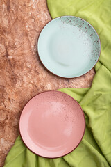 Two empty blue and pink plates on brown concrete background and green textile. Top view.