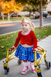 © Brocreative - Disability photo of a cute little disabled girl walking with a special walker outdoors on the sidewalk