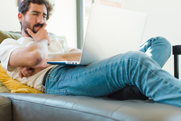 Poster - young bearded man resting on a couch with a laptop