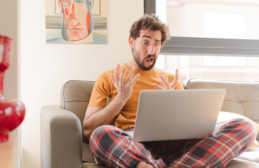 Wall Mural - young bearded man looking desperate and frustrated, stressed, unhappy and annoyed, shouting and screaming and sitting with a laptop