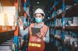 © APchanel - Industry manager and worker under checking about production at factory warehouse by tablet. They wearing safety uniform hard hat ,face mask to protect virus in new normal concept.