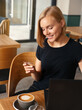 Beautiful blond woman using credit card for online payment on laptop while drinking coffee in cafe