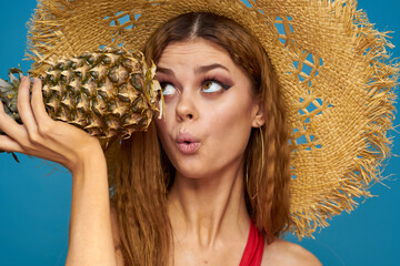 A woman in a straw hat with a pineapple in her hands or is it a fun blue exotic fruits background