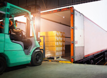 Forklift Tractor Loading Packaging Boxes Into Cargo Container. Cargo Trailer Truck Parked Loading At Dock Warehouse. Shipment Delivery Service. Shipping Warehouse Logistics.  Freight Truck Transport.	