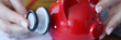 Woman listening with stethoscope to red piggy bank closeup