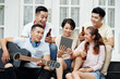© DragonImages - Group of Asian friends drinking beer and singing songs while playing guitar during a party