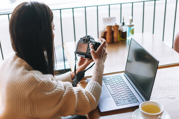 Brunette smiling young woman photographer working with her camera and laptop in cafe