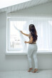 © nuzza11 - Beautiful woman holds a curtain near the window. The woman looks out the window. High quality photo