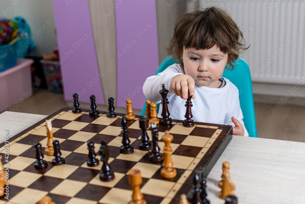Mała dziewczynka z szachownicą. Dziecko uczy się grać w szachy. - obrazy, fototapety, plakaty 