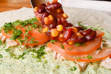 Wall Mural - Burrito making process. The cook adds beans and corn in tomato sauce to meat, herbs and tomatoes on pita with sauce. Mexican dish.