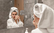 © puhimec - A young woman in a robe and with a towel on her head is putting patches under her eyes.
