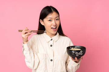 Wall Mural - Young asian woman isolated on pink background holding a bowl of noodles with chopsticks