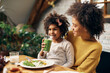 © Drazen - Happy African American girl drinking smoothie while having meal with mother at home.
