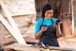 © Confidence - female african carpenter using her phone and credit card, paying online