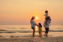 Happy Asian Family That Enjoys Beach Activities During The Summer Holidays. Parent And Children Enjoy The Sunset Sea On Beach.Holiday Travel Concept, Summer Vacations.