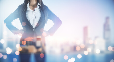 Wall Mural - Success concept with businesswoman in black suit with hands on the belt and blurry city background