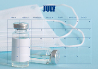 Wall Mural - Clean desktop calendar for the month of July. The layout used as the schedule planner. An ampoule with a vaccine, a mask, a medical syringe in the background. All inscriptions are in English