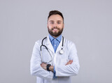 Fototapeta Na sufit - Portrait of positive male doctor posing with crossed arms and smiling at camera over grey studio background