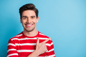 Poster - Photo of happy cheerful young man point index finger empty space advert isolated on blue color background