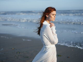 Charming woman in a sundress near the ocean on the shore of the beach model red hair