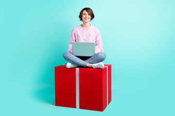 Photo of sweet impressed young lady dressed purple pullover sitting red present writing modern device isolated teal color background