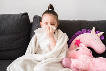 runny nose, a little girl is being treated at home. toddler girl sits on the couch and blows her nos