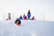 © absphotography/Stocksy - Cute child happily riding down a hill on a toboggan sled with his dad. Interracial family