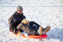 Cute Child Happily Riding Down A Hill On A Toboggan Sled With His Dad. Interracial Family