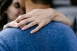 © Léa Jones/Stocksy - hand with engagement ring on fiancé's neck.