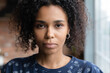 Close up portrait of beautiful confident millennial african american woman with perfect fresh healthy face skin black curly hair. Attractive young mixed race female looking at camera posing indoors