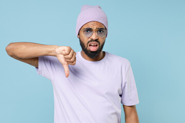 Wall Mural - Young displeased dissatisfied unshaven student black african man 20s wear violet t-shirt purple hat glasses showing thumb down dislike gesture isolated on pastel blue color background studio portrait.