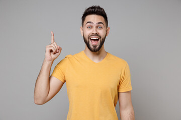 Wall Mural - Young caucasian bearded happy insighted smart intelligent man 20s wearing casual yellow basic t-shirt holding index finger up with great new idea isolated on grey color background studio portrait.