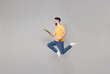 © ViDi Studio - Full length of young bearded cool student frelancer man in yellow basic t-shirt jump high holding laptop pc computer chatting browsing by fast internet isolated on grey background studio portrait.