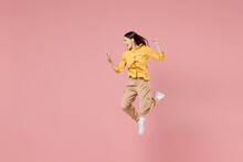 Full Length Side View Of Young Brunette Overjoyed Latin Woman 20s In Yellow Shirt Hold Mobile Cell Phone Jump High Do Winner Gesture Clench Fist Isolated On Pastel Pink Background Studio Portrait.