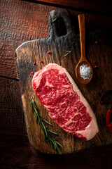 Poster - Raw striploin steak (New York) of beef on a seasoning board. Rustic style with wooden old background, top view