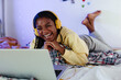 © BONNINSTUDIO/Stocksy - Happy black teenager watching movie on bed