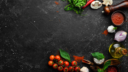 Wall Mural - Kitchen cooking background: cherry tomatoes, onions, spices and herbs. On a black background.