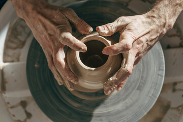 Professional potter working with clay on potter's wheel in workshop or studio