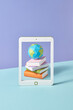 © Yaroslav Danylchenko/Stocksy - Papercraft tablet screen with books and globe.