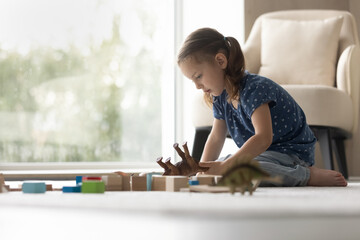 Wall Mural - Small Caucasian girl child sit on floor in living room play with animal figures on weekend. Cute little 8s kid have fun relax alone at home, involved in playful game activity. Entertainment concept.