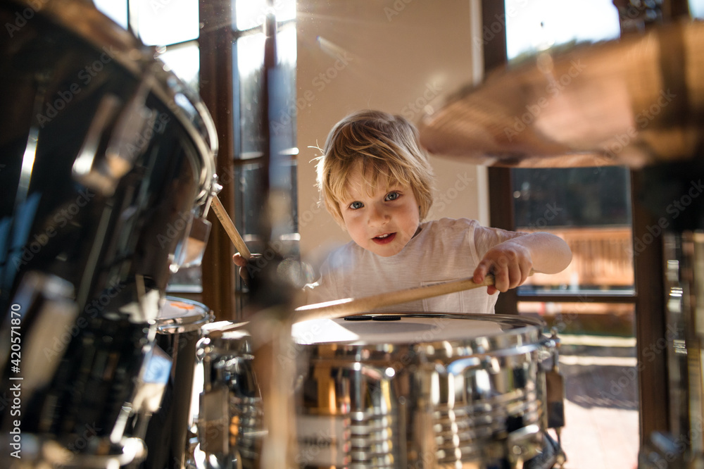Front view of small boy indoors at home, playing drums. - obrazy, fototapety, plakaty 