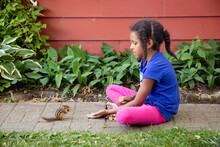 A Young Child Sitting In Front Of A Trail Of Peanuts While A Chipmunk Approaches
