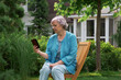 © Dmitry Borovikov/Stocksy - Beautiful elderly woman in her garden communicates online on a smartphone