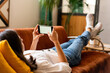 © Malquerida Studio/Stocksy - Young woman at home lying down in the couch using smartphone .