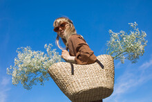 Blonde Girl In Red Glasses Holds A Basket Of Flowers Against The Sky