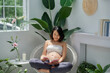 © Maki Company Limited/Stocksy - beautiful pregnant young woman on armchair and reading a book in white apartment interior with many fresh plants
