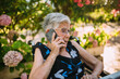 © MyMicrostock/Stocksy - Happy elderly woman talking on phone using a modern laptop
