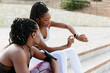 © Jimena Roquero/Stocksy - Two women friends sitting on stairs checking a smart watch on one of them's wrist.
